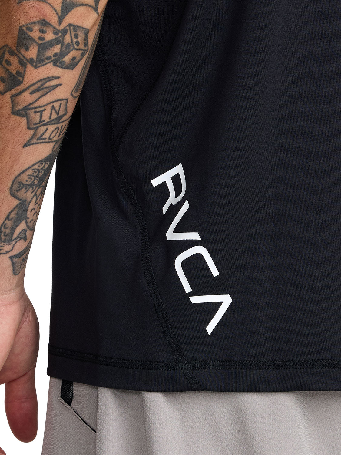 Black short-sleeve polo shirt with a black RVCA logo printed vertically near the lower left side. Back Close Up View
